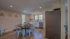 Una cocina con piso de madera, una mesa de comedor con sillas, un refrigerador y una ventana con vistas.