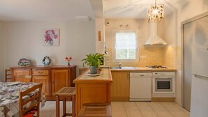 A compact kitchen with a dining area, featuring a wooden table, chairs, a potted plant, a sink, a stove, and a dishwasher.