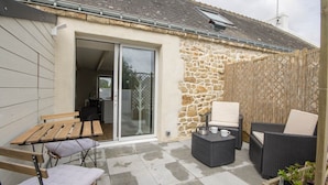 A patio with a stone wall, a sliding glass door leading to a room, and outdoor furniture including a table and chairs.