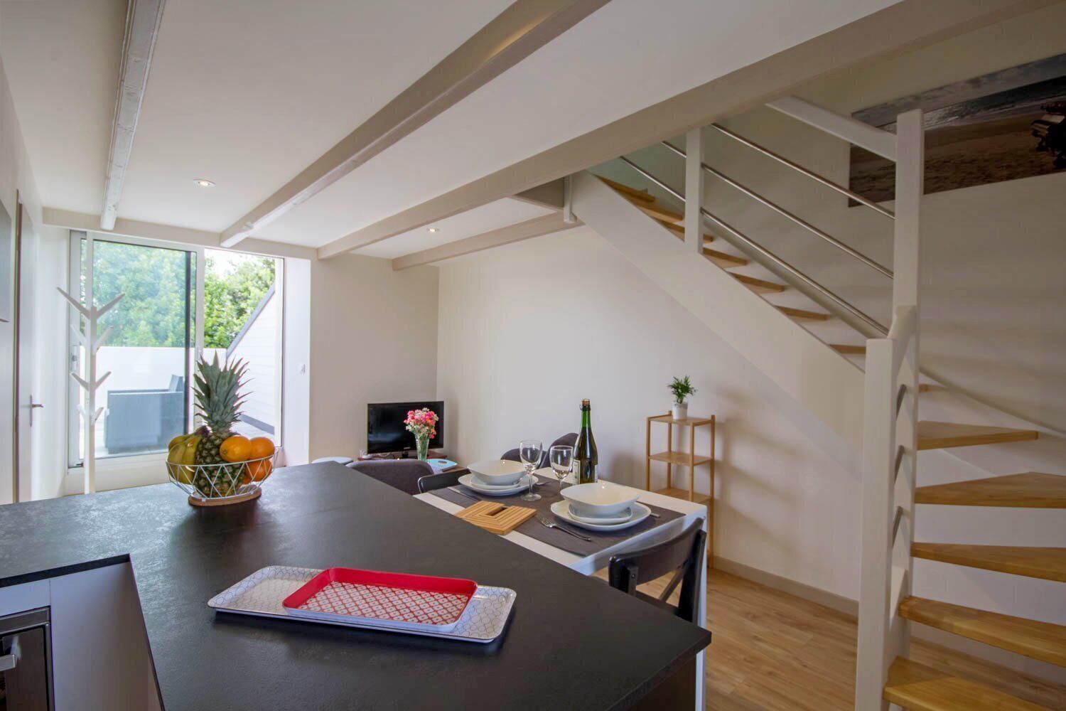 A modern dining area with a black table, white chairs, and a wooden staircase.