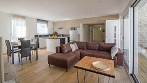En moderne lejlighed med spiseområde, stue med brun lædersofa, køkken og stor skydedør til en stenvæg.