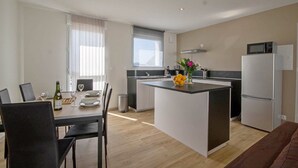 Et moderne køkken med en central ø, et spiseområde med bord og stole, samt en opholdsstue med sofa.