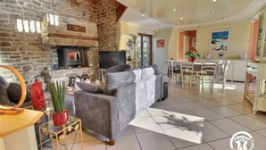 Un salon avec une cheminée en pierre, un téléviseur, un canapé et un coin repas comprenant une table et des chaises.