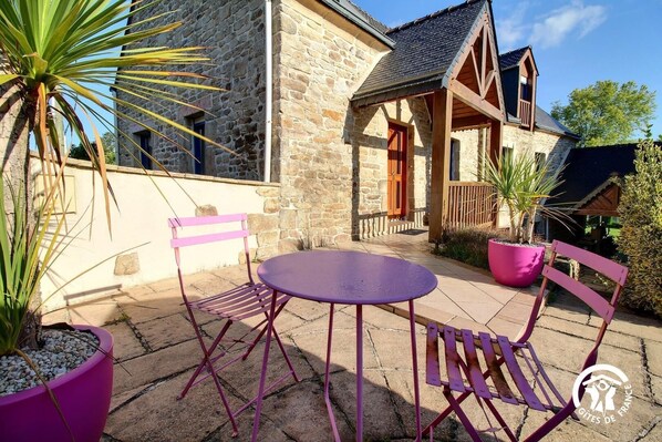 A stone building with a balcony, a purple table, and two purple chairs. - Le Gîte du Procureur (MONTERBLANC)