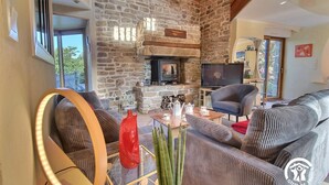 Un salon chaleureux avec une cheminée en pierre, un téléviseur et des fauteuils confortables.