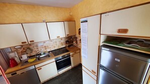 Una cocina compacta con armarios blancos, un refrigerador de acero inoxidable y un horno negro.
