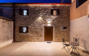 A stone building with a wooden door, two windows, and a small table with chairs.