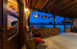 A cozy outdoor seating area with a brick wall, a wooden ceiling, and hanging flower baskets.
