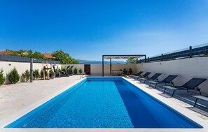 A swimming pool with exercise equipment, lounge chairs, and a view of mountains.