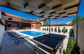 A swimming pool with lounge chairs, a table, and exercise equipment under a covered area.