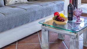 A living room with a grey sofa, a glass coffee table with a bowl of fruit and a bottle of wine, and a purple glass on the table. - CSC - 5 - Baia de Bahas by Interhome (Golfo di Marinella)