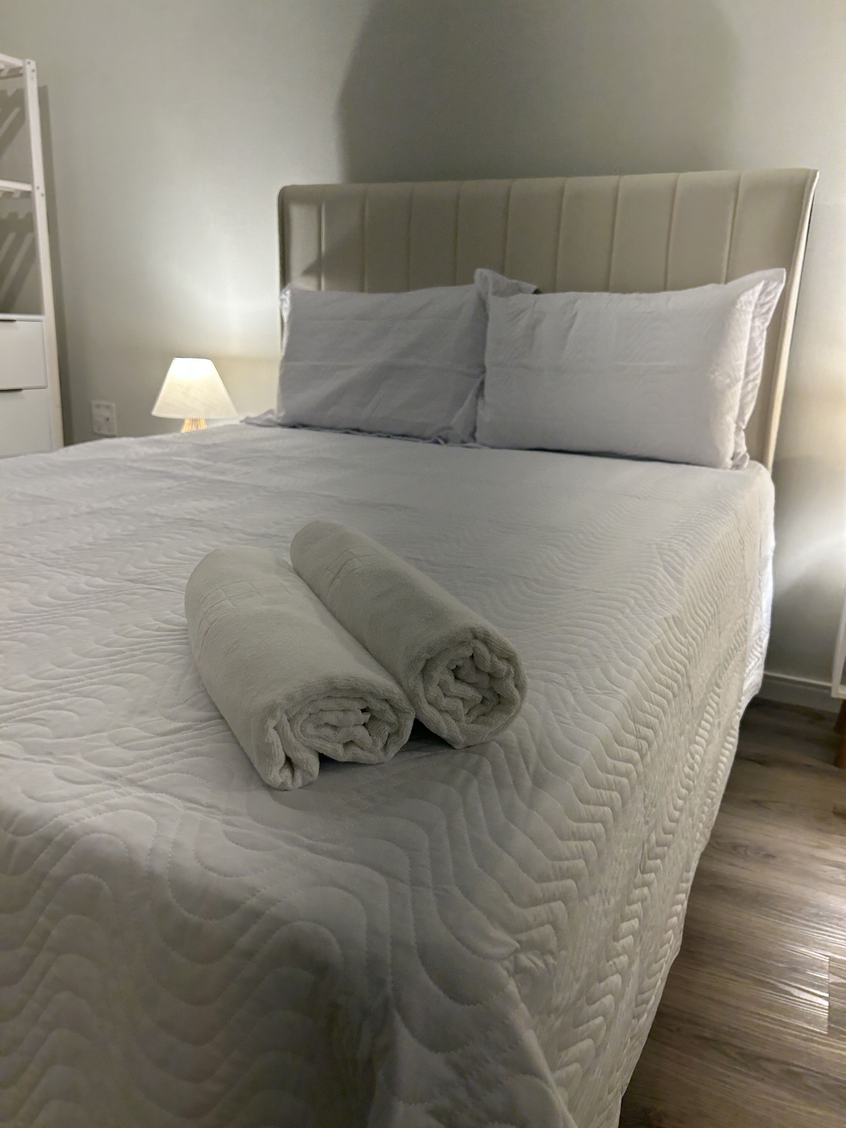 Una cama bien hecha con una colcha acolchada, dos almohadas y dos toallas enrolladas sobre la cama.