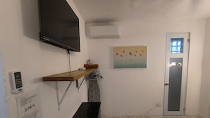 Un baño con una banca de madera, un televisor montado, un equipo de aire acondicionado, una puerta con ventana y un perchero de toallas en la pared.