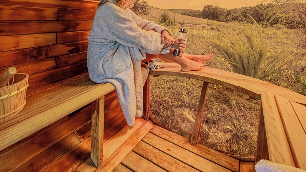 Une cabane en bois dotée d’une lucarne circulaire, d’un banc et d’une table sur laquelle se trouvent une serviette et un seau.