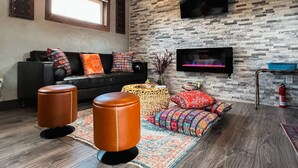 Un salon avec un canapé en cuir noir, des coussins à motifs, une table basse et un téléviseur à écran plat fixé à un mur dont la texture rappelle celle de la pierre.