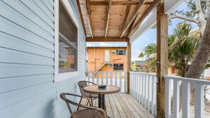 A wooden deck with a table and chairs, a white railing, and a view of a building in the background.
