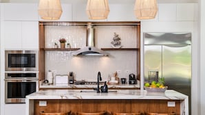 Una cocina moderna con una isla central, taburetes de bar, electrodomésticos de acero inoxidable y elementos decorativos.