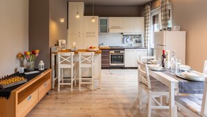 A modern kitchen with white cabinets, a wooden countertop, and a dining area with white chairs. - Graziella by Interhome (Leggiuno)