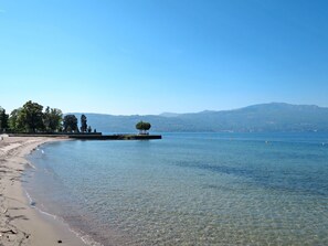 Ein klarer See mit Sandstrand und einer kleinen Insel mit Bäumen.