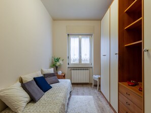 Ein Schlafzimmer mit Bett, Heizkörper, einem Fenster mit Vorhängen, einem Nachttisch und einem Kleiderschrank.
