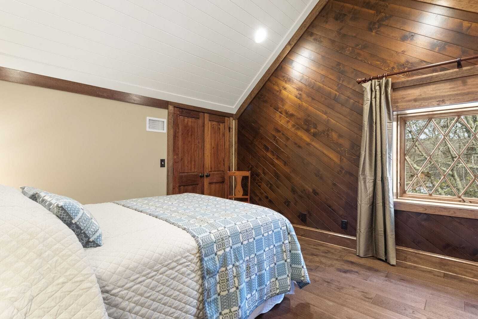 A bedroom with a bed, wooden walls, a window, and a door.