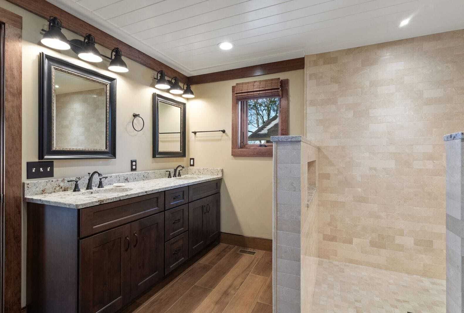 A bathroom with a double vanity, two large mirrors, a window with a view, and a stone accent wall.