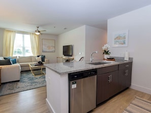 A modern kitchen with a built-in dishwasher, a dining area with a sofa, and a television.