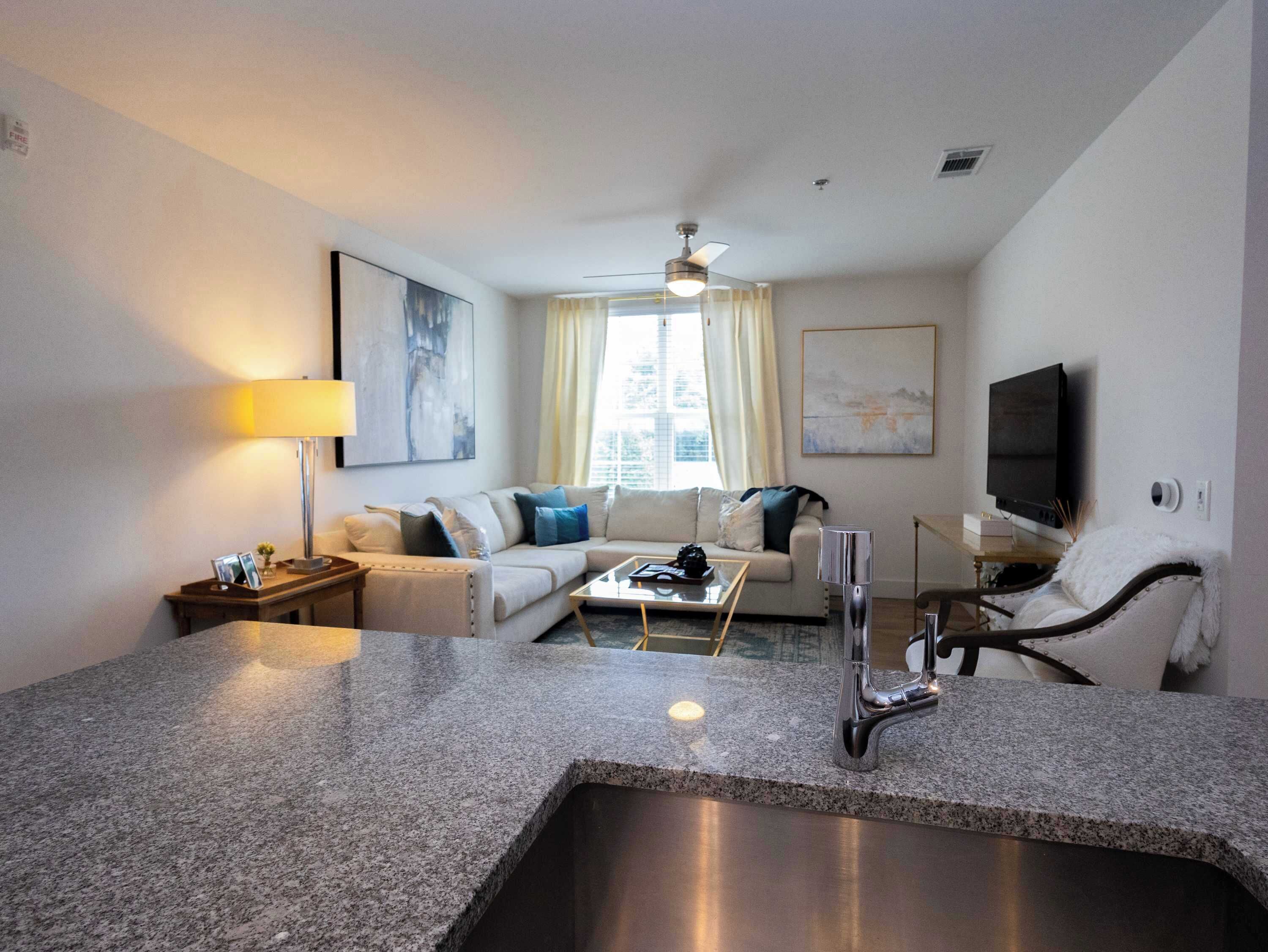 Una habitación de hotel moderna con área de cocina, un conjunto de sofá, un televisor de pantalla plana y un ventilador de techo.