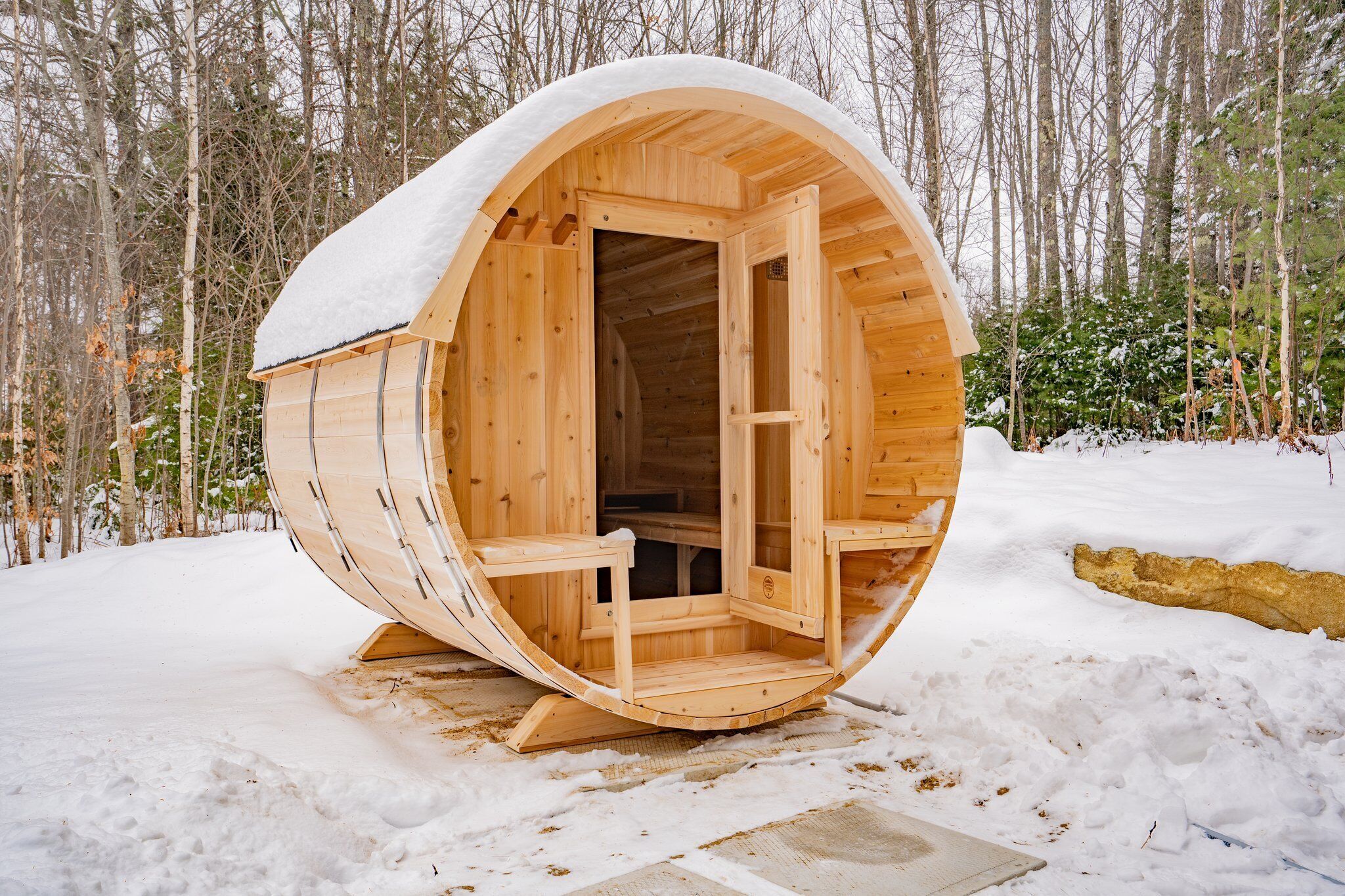 Una estructura cilíndrica de madera cubierta de nieve, con una puerta abierta, en un bosque nevado.