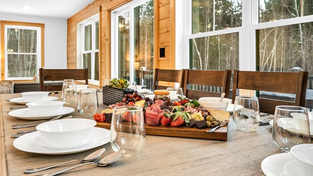 A dining table set with plates, cutlery, and a charcuterie board with various cheeses, fruits, and meats. - NEW Chalet 6 minutes from Sunday River! Hot tub, Sauna, Sleeps 12, Dog Friendly! (Bethel)