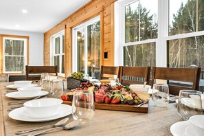 Una mesa de comedor dispuesta con platos, cubiertos y una tabla de embutidos con varios quesos, frutas y embutidos.