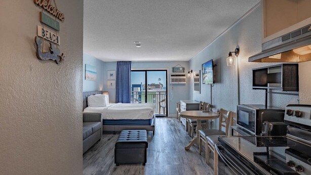 A compact hotel room with a bed, a sofa, a dining table, and a kitchenette. - Coastal Retreat with Ocean Views | Driftwood 1608 (Myrtle Beach)