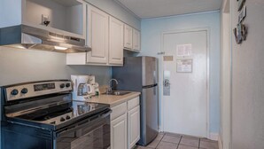 A compact kitchen with a stove, oven, refrigerator, and white cabinets. - Coastal Retreat with Ocean Views | Driftwood 1608 (Myrtle Beach)
