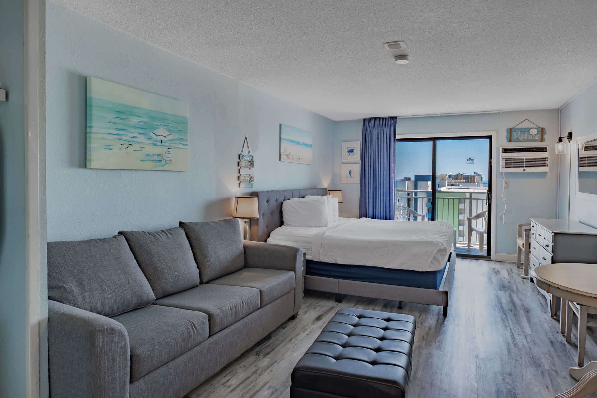 A hotel room with a bed, a sofa, a small table, and a balcony with a view.
