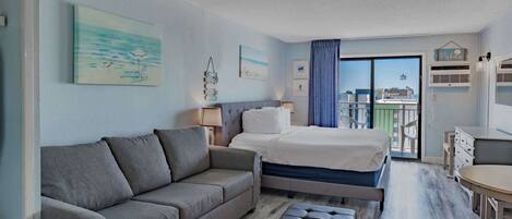 A hotel room with a bed, a sofa, a small table, and a balcony with a view.