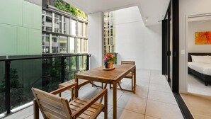 Un balcon avec une table et des chaises en bois, une vue sur la verdure et un intérieur moderne comprenant un lit et des œuvres d’art.