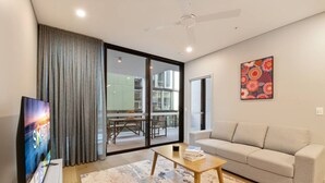 Un salon moderne avec un canapé, une table basse, un téléviseur et une grande fenêtre avec des rideaux.