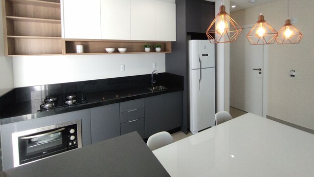 A modern kitchen with a built-in oven, a refrigerator, and a dining table with chairs. - Refúgio Praiano em Bombinhas (Centro Bombinhas)