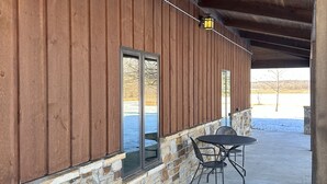 Un espacio al aire libre techado con pared de piedra y madera, una mesa con sillas y vista a un paisaje nevado.