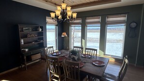 Un comedor con una mesa de madera dispuesta para seis personas, rodeada de sillas. Un candelabro cuelga del techo y hay un aparador oscuro contra la pared.