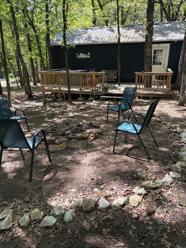 Een rustieke buitenruimte met houten banken en stoelen, omgeven door bomen en een stenen pad.