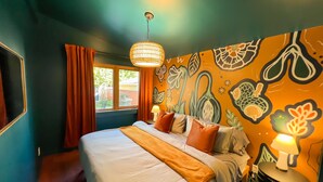 Une chambre à coucher avec un lit, des rideaux, une fenêtre et un mur décoré d’une fresque représentant des plantes.