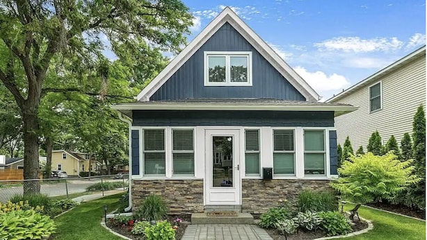 Une maison à deux étages avec une façade en pierre, un porche à l’avant et une pelouse bien entretenue.