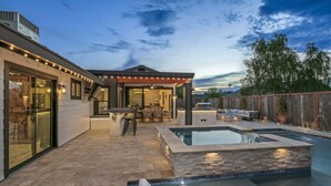 A modern outdoor pool area with a hot tub, a covered seating area, and a patio with outdoor furniture.