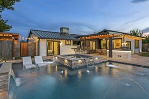 A modern outdoor pool area with a hot tub, lounge chairs, and a barbecue area.