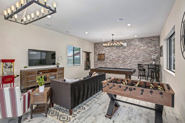 A modern living room with a foosball table, a TV, and a brick wall.