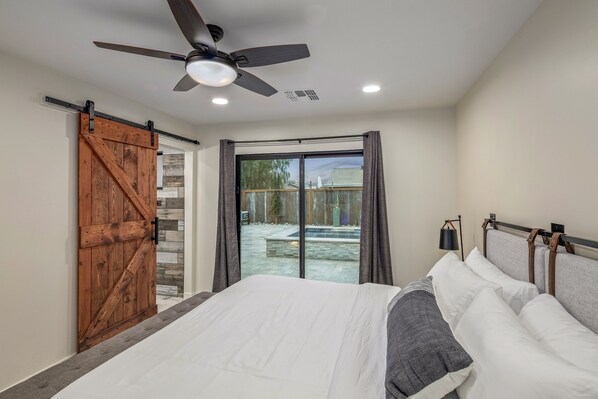 A bedroom with a bed, a ceiling fan, and a view of a backyard through a sliding glass door.