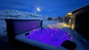 A hot tub with purple lights in a snowy outdoor setting at night.