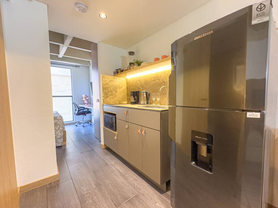 Una cocina moderna con un refrigerador de acero inoxidable, una cafetera integrada y un lavamanos pequeño.