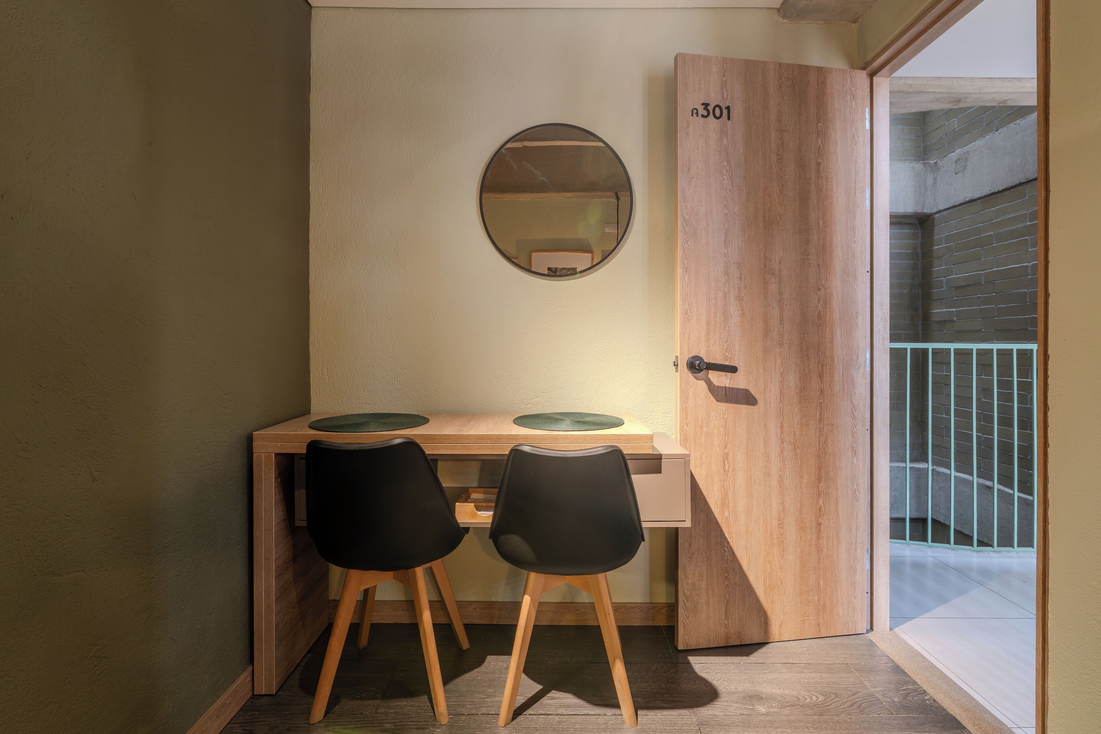 A compact workspace with two chairs, a wooden desk, a round mirror, and a door marked with the number 301.
